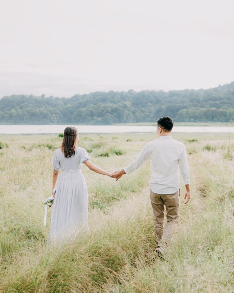 a man and woman holding hands walking through tall grass